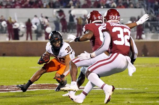 Oklahoma State running back Chuba Hubbard (30) slips in front of Oklahoma cornerback Tre Brown (6) and safety Delarrin Turner-Yellan (32) during the first half of an NCAA college football game in Norman, Okla., Saturday, Nov. 21, 2020. (AP Photo/Sue Ogrocki)
