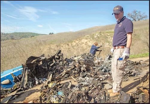 NTSB INVESTIGATORS Adam Huray, right, and Carol Hogan examine wreckage as part of the NTSB’s investigation of a helicopter crash near Calabasas, Calif. The Sunday crash killed nine persons, including former NBA basketball player Kobe Bryant and his 13-year-old daughter, Gianna, (James Anderson/National Transportation Safety Board via AP)
