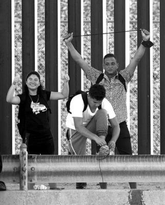 Venezuelan migrants gesture as they reach the U.S. border fence to turn themselves into the U.S. Border Patrol after crossing the Rio Grande from Mexico on September 22, 2022, in El Paso, Texas.
