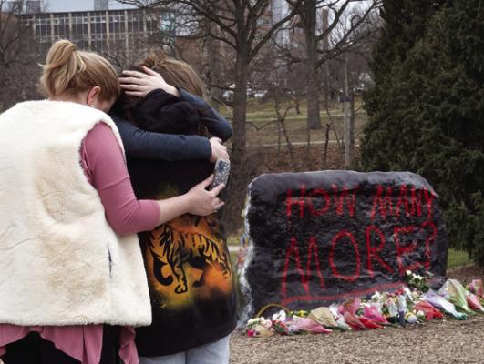 People leave flowers, mourn and pray at a makeshift memorial at “The Rock” on the campus of Michigan State University on Feb. 14, 2023, in Lansing, Mich. A gunman opened fire at two locations on the campus last night killing three students and injuring several others. (Scott Olson/Getty Images/TNS)
