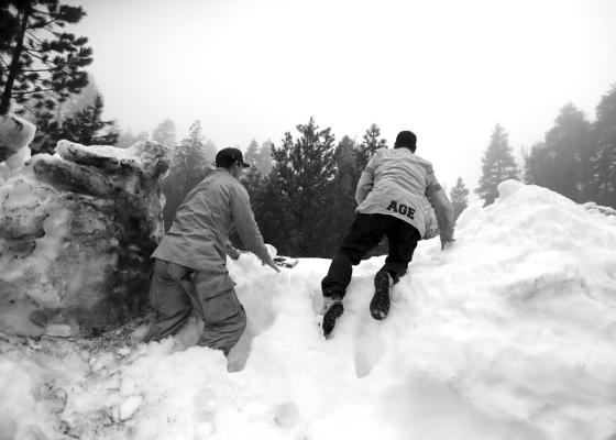 Firefighters Aaron Thomas, left, and medic Mike Age climb a steep snow berm as they attempt to deliver prescription medicine to a snowed-in San Bernardino mountain resident on Friday in Lake Arrowhead, California. (Brian van der Brug/Los Angeles Times/TNS)