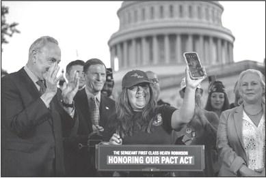 From left, Senate Majority Leader Chuck Schumer (D-New York) looks on as Rosie Torres, wife of veteran Le Roy Torres, who suffers from illnesses related to his exposure to burn pits in Iraq, holds up her husband Le Roy on her phone after the Senate passed the PACT Act at the U.S. Capitol Aug, 2, 2022, in Washington, D.C. (Drew Angerer/Getty Images)