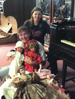 Surrounded by part of the Top of Oklahoma Museum’s extensive doll collection is Jai Rogers with Director Melissa Hudson looking on. Rogers’s work at the Museum is underwritten by a grant from the Oklahoma Historical society. Courtesy photo.