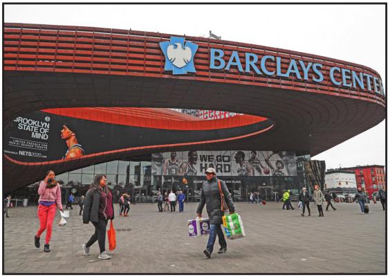 PEDESTRIANS WALK past the Barclays Center, which is home to the Brooklyn Nets, in the Brooklyn borough of New York. The Nets announced on Tuesday that four players have tested positive for the new coronavirus, bringing the total to seven known players in the NBA. (AP Photo)