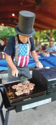 Chef Charley Bottger, Ponca City gets into the mood with the red, white and blue theme as he flips hamburgers during the Wheeler Dealers Camping Club June campout at Blue Bill Point.