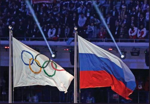 THE RUSSIAN NATIONAL flag, right, flies after next to the Olympic flag during the closing ceremony of the 2014 Winter Olympics in Sochi, Russia. The World Anti-Doping Agency banned Russia on Monday from the Olympics and other major sporting events for four years, though many athletes will likely be allowed to compete as neutral athletes. (AP Photo)