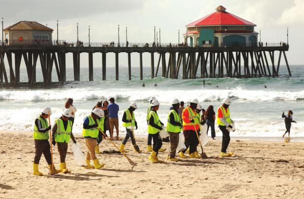 Workers comb the Huntington Beach shoreline on Monday. (Al Seib/Los Angeles Times/TNS)