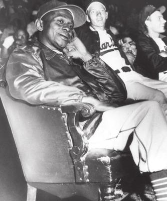 SATCHEL PAIGE sits in a chair outside the dugout because of his “advanced age.”