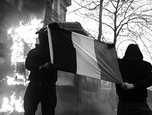 Protesters hold a French flag next to a burning news kiosk beside the Place de l’Opera on the sidelines of a demonstration as part of a national day of strikes and protests, a week after the French government pushed a pensions reform through parliament without a vote, using article 49.3 of the constitution, on March 23, 2023, in Paris. (Alain Jocard/AFP/Getty Images/TNS)