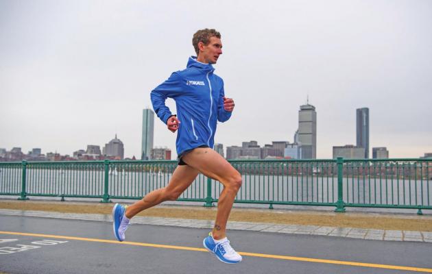 IN THIS 2019 photo provided by Hoka One One, Tyler Andrews runs along the Charles River in Cambridge, Mass., with he Boston skyline in the background. Andrews isn’t among the favorites at the Olympic Marathon trials this weekend in Atlanta. Don’t be surprised, though, should he make a run at a spot on the U.S. team for the Tokyo Games. (Hoka One One via AP)