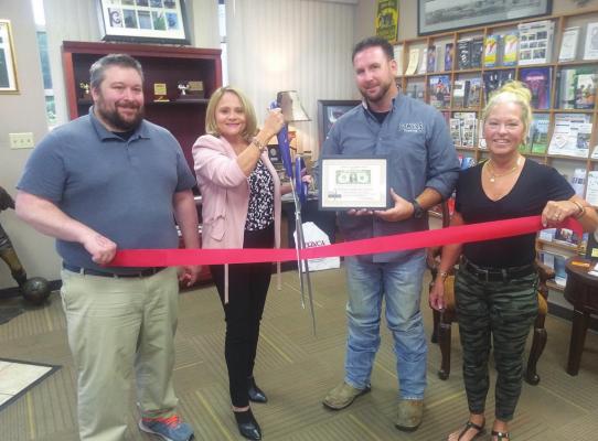 THE CHAMBER held a Ribbon Cutting Ceremony for Triangle Insurance Cooperative Service. Brenda Rogers, the owner, cuts the ribbon. Holding the ribbon are Matt Duplissey and Kim Hancock. Garrett Bowers presents Brenda with her first dollar return on investment.