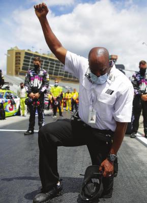 A NASCAR official kneels during the national anthem before a NASCAR Cup Series auto race at Atlanta Motor Speedway, Sunday, June 7, 2020, in Hampton, Ga. NASCAR paused before Sunday’s Cup race at Atlanta Motor Speedway to acknowledge the country’s social unrest. (AP Photo/Brynn Anderson)