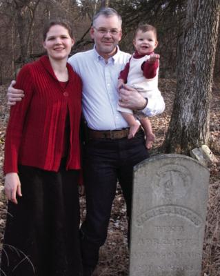 Elizabeth Pruett, daughter Anna, and father Robert Moore stand by 1877 tombstone of James Woods, husband of Cyrena.