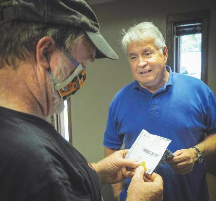 JOHN HOLMAN, director of OSU Extension in Murray County, masked, receives strange seeds from gardener Robert Tucker in Tucker’s office. (Photo by Todd Johnson, OSU Agricultural Communications Services)